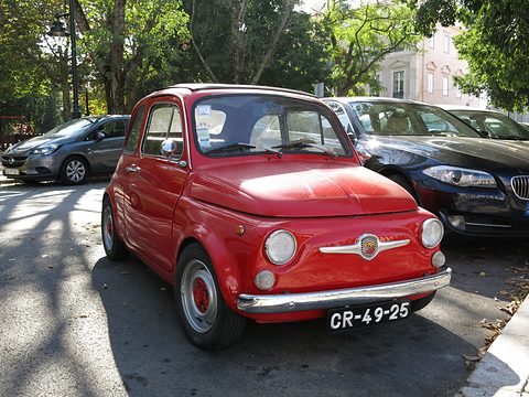 Red Fiat 500 with an Abarth moustache badge and red wheels, parked under trees in dappled shade. Opens a larger view