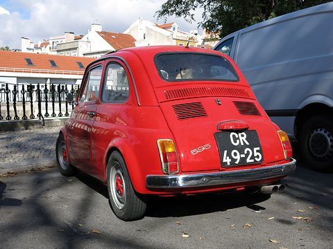 Rear of a red Fiat 500 with a 595 badge, Portuguese plate and twin tailpipes, a white van beside it. Opens a larger view