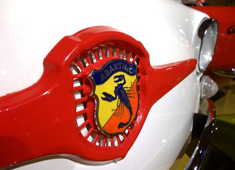Red moustache trim on white paint around an enamel shield with a blue scorpion on yellow and orange. Opens a larger view