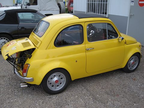 Yellow Fiat 500 seen from the left rear with the engine lid raised on a bracket and wide alloy wheels.