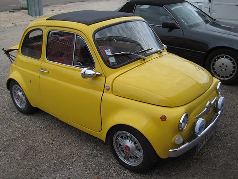 Yellow Fiat 500 with a black roof, flared wheel arches and alloy wheels, parked on gravel beside a black car. Opens a larger view
