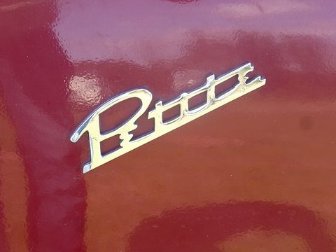 Close view of a chrome script badge reading Petite on glossy maroon paint. Opens a larger view