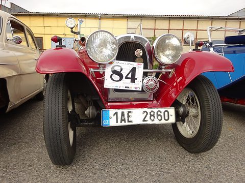 Front view of a red roadster with large headlamps, race number 84 and plate 1AE 2860 on tarmac.