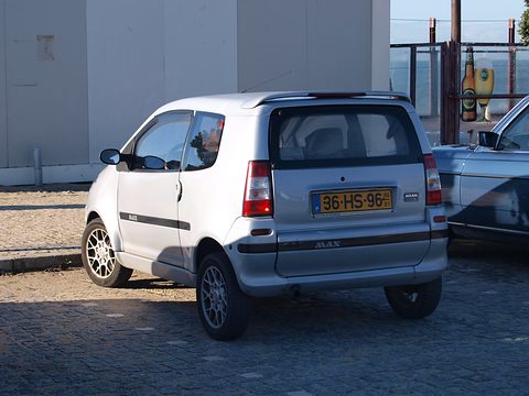 Silver small hatchback from the rear with a yellow Dutch plate and MAX lettering on the bumper, parked on cobbles. Opens a larger view