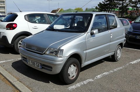 Silver boxy small hatchback with a slatted grille and plate FE-598-GA, parked between modern cars. Opens a larger view