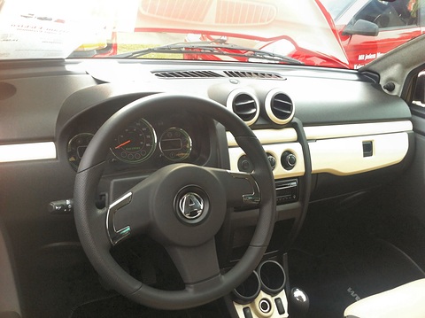 Black and cream dashboard with a three-spoke wheel, twin round vents and two dials, seen through the open door. Opens a larger view