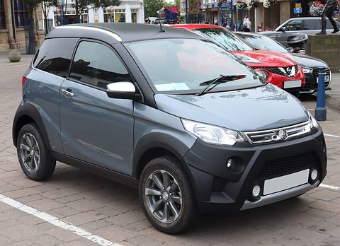 Blue-grey small crossover with black lower body, chrome grille bar and a blank pale plate, parked on paving. Opens a larger view