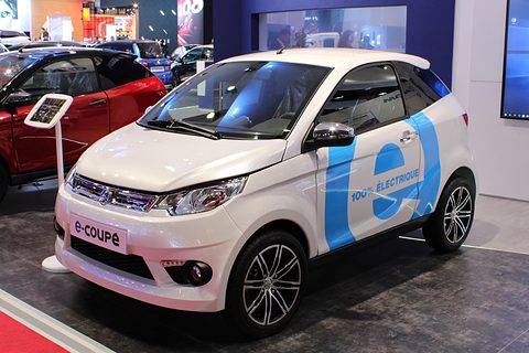 White small coupé with large blue e graphics and 100% ÉLECTRIQUE lettering on its door, on a show stand.