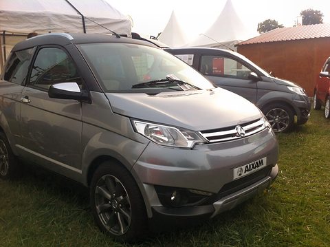 Grey small estate with a chrome grille, roof bars and an AIXAM plate, parked on grass beside a marquee. Opens a larger view