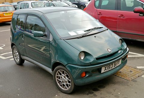 Dark green rounded small hatchback with a British plate X193 BNY, parked across a car-park bay beside a red car. Opens a larger view