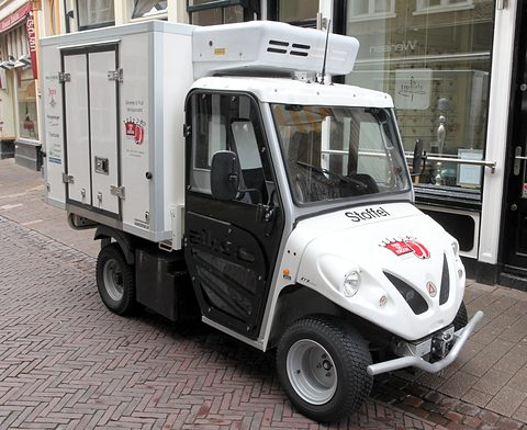 White small electric utility truck with a refrigerated box body and roof unit parked on brick paving.