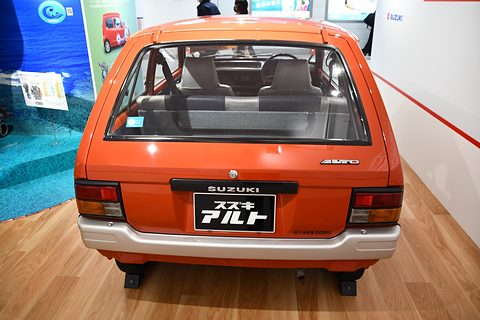 Rear of an orange small hatchback with a large hatch window, small tail lamps, a white bumper and a Japanese show plate.