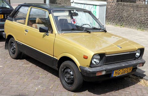 Gold small three-door hatchback with a black roof, black wheels and a Dutch plate, parked on brick paving. Opens a larger view