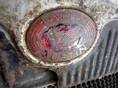 Close view of a worn oval badge reading American Austin on a corroded radiator shell. Opens a larger view