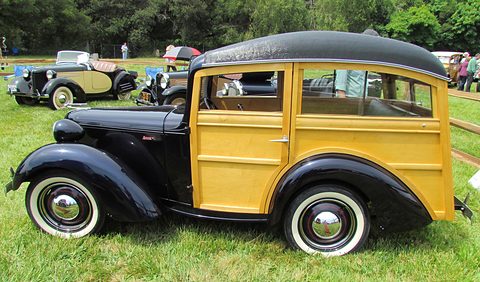 A small station wagon with a black bonnet and wings and a varnished wooden body on a lawn. Opens a larger view
