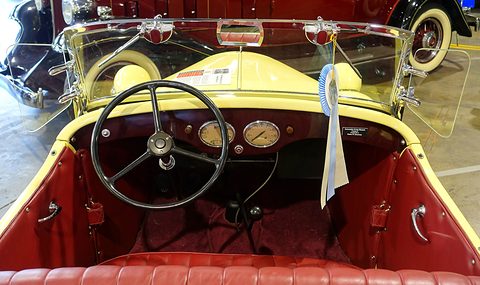 Looking down into a yellow open car with red seats, a black steering wheel and a ribbon on the windscreen. Opens a larger view