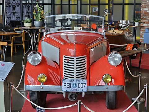 Head-on view of a red roadster with a vertical-bar grille, headlamps in the wings and a white bumper behind a rope. Opens a larger view