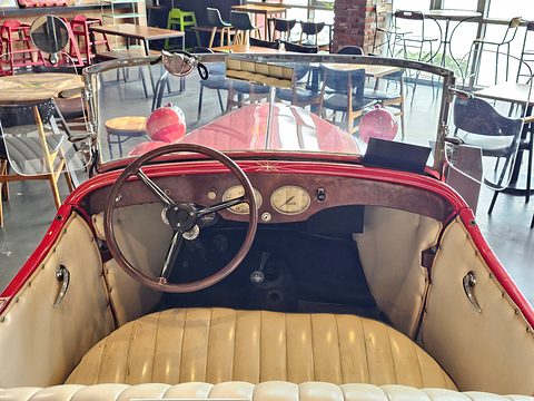 Looking into a red open car over a cream bench seat to a thin steering wheel and dials in a red dashboard. Opens a larger view