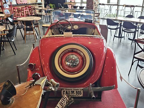 The rear of a red roadster with a white-walled spare wheel on its tail and a number plate below. Opens a larger view