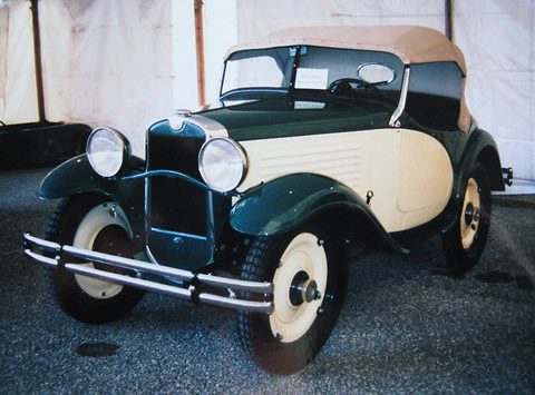 A small two-tone coupé with a dark green top and cream body, white-wall tyres and chrome bumper indoors. Opens a larger view