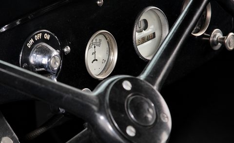 Close view of a black dashboard with three round cream dials, an ignition switch and a spring-spoke steering wheel. Opens a larger view