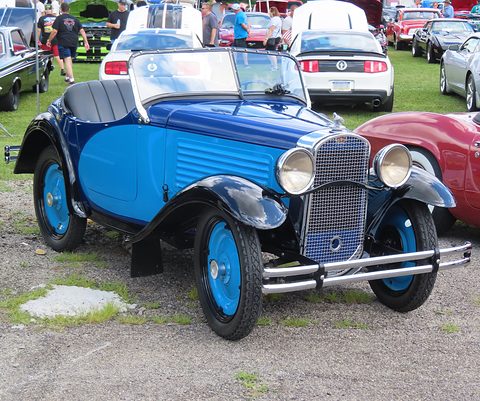 A small light-blue open two-seater with dark blue wings and light blue wheels in a car park. Opens a larger view
