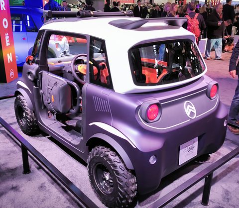 Rear of a lilac and white open two-seater with round red tail lamps and chunky tyres, a crowd behind. Opens a larger view