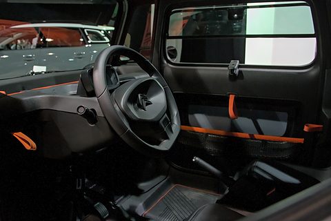 Bare black dashboard with a small steering wheel, a phone clip and orange straps on the door, seen through the open door. Opens a larger view