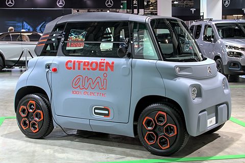 Grey cube-shaped two-seater with orange wheel inserts and red Citroën ami lettering on its side, on a show floor.