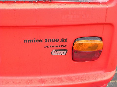 Black lettering reading amica 1000 S1 automatic and a small bma logo beside an orange and red tail lamp on red plastic.