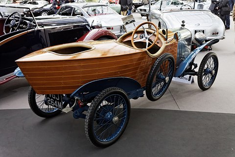 Rear quarter view of a car with a planked wooden boat-shaped tail, blue wings and blue wire wheels. Opens a larger view