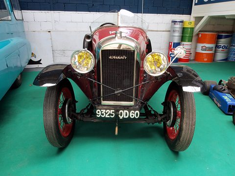 Front view of a maroon open car with yellow-lensed headlamps, a chrome radiator and number plate 9325 QD 60 on a green floor. Opens a larger view