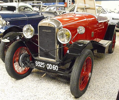 A red open car with black wings, a chrome radiator, two headlamps and red wire wheels, other cars close behind. Opens a larger view