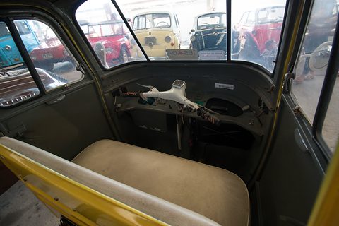 Cream bench seat behind a handlebar steering column and a bare metal dashboard, seen through the open door. Opens a larger view