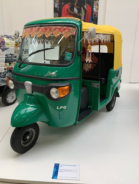 Green and yellow three-wheeled taxi with tasselled decorations inside, an LPG badge and a black canvas roof. Opens a larger view