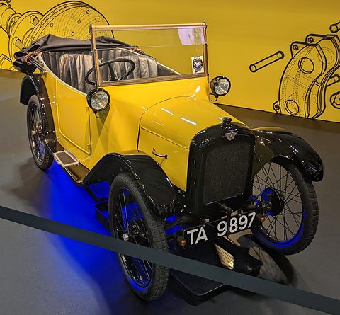 A yellow open tourer with black wings and hood on a show stand, blue lights glowing on its wheels. Opens a larger view