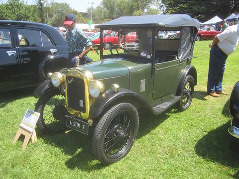 A small green open tourer with black wings and wire wheels on grass, a man in a cap behind it. Opens a larger view