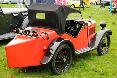 The rounded orange tail of a two-seater with a black hood up and a number plate. Opens a larger view