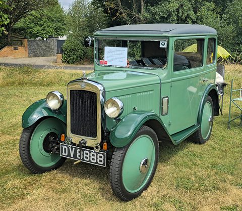 A pale green square-roofed saloon with dark green wings and wheels on grass under trees. Opens a larger view