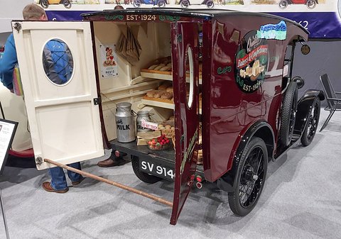 A maroon van with its back doors open on trays of loaves, a visitor at the left edge. Opens a larger view