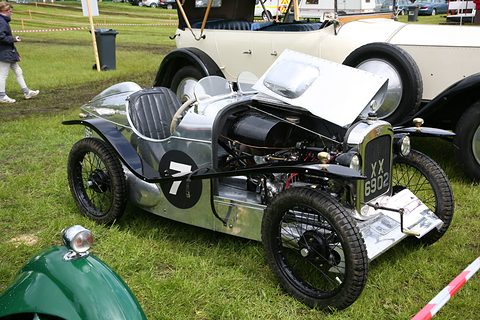A polished aluminium sports two-seater with its bonnet raised and wire wheels on grass. Opens a larger view
