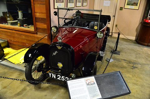 A red open tourer with black wings behind a chain in a museum, an information board on the floor. Opens a larger view