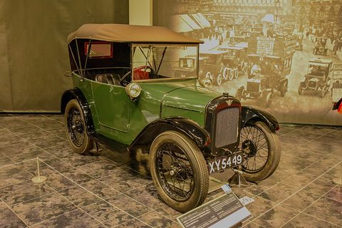 A green open tourer with a tan hood up, black wings and wire wheels on a tiled museum floor. Opens a larger view