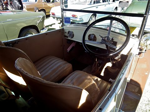 Looking over the side of an open car at pleated brown leather seats and a big black steering wheel. Opens a larger view