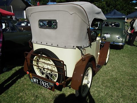 The rear of a cream open tourer with its fabric hood up and a spare wheel on a luggage rack. Opens a larger view