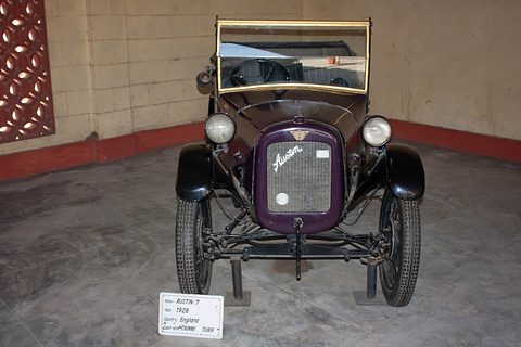 A small dark tourer seen head-on with a purple-faced radiator and its windscreen up, a placard in front. Opens a larger view