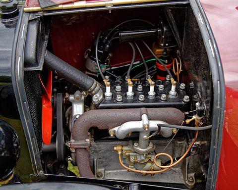 Close view of a small side-valve four-cylinder engine with its plugs, pipes and red bonnet sides. Opens a larger view