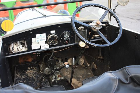 Looking into a small open car at a large steering wheel and a central instrument panel above the pedals. Opens a larger view