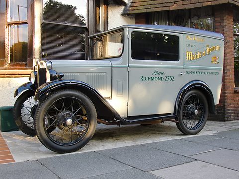 A pale green van with gold lettering parked outside a shop with timber-framed windows. Opens a larger view