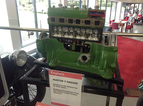 A green four-cylinder engine block with its valve gear exposed on a stand above an explanatory sign. Opens a larger view